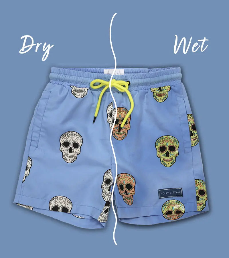 Holly and Beau Colour changing Light Blue swim shorts with skull patterns on a blue background, showing 'Dry' and 'Wet' text and wet and dry sides