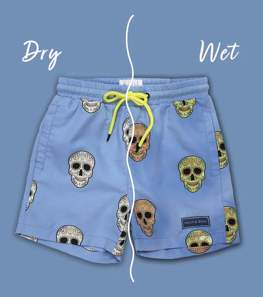 Holly and Beau Colour changing Light Blue swim shorts with skull patterns on a blue background, showing 'Dry' and 'Wet' text and wet and dry sides